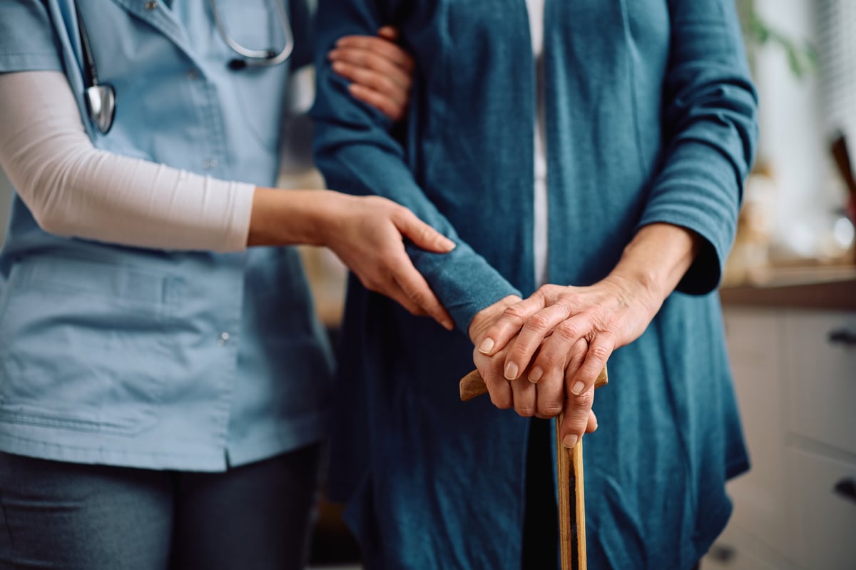 Close up of an elderly woman with a walking cane and a visiting caregiver