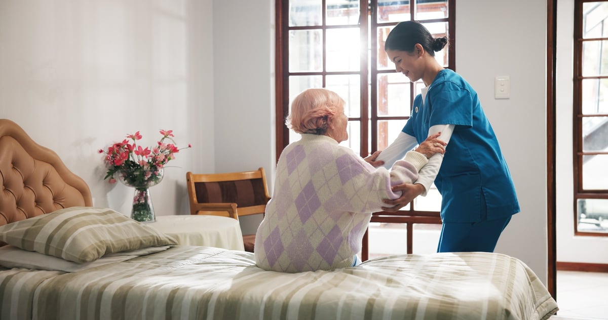 A caregiver helping a resident with mobility support in her bedroom