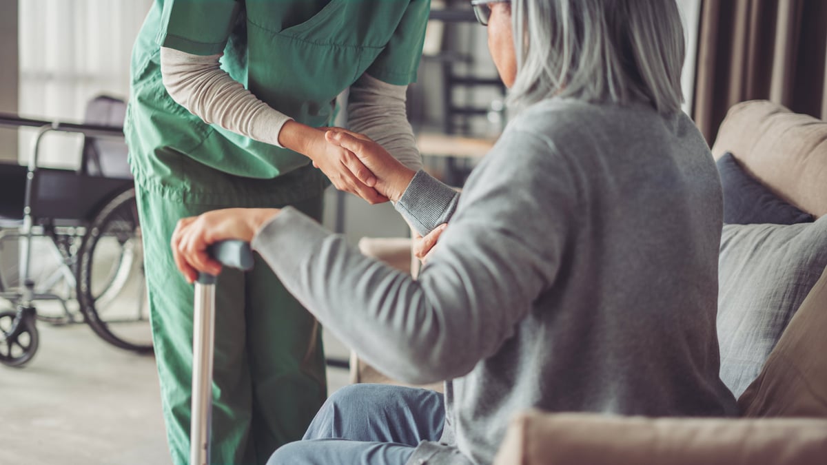 A caregiver assisting an elderly resident who is using a cane